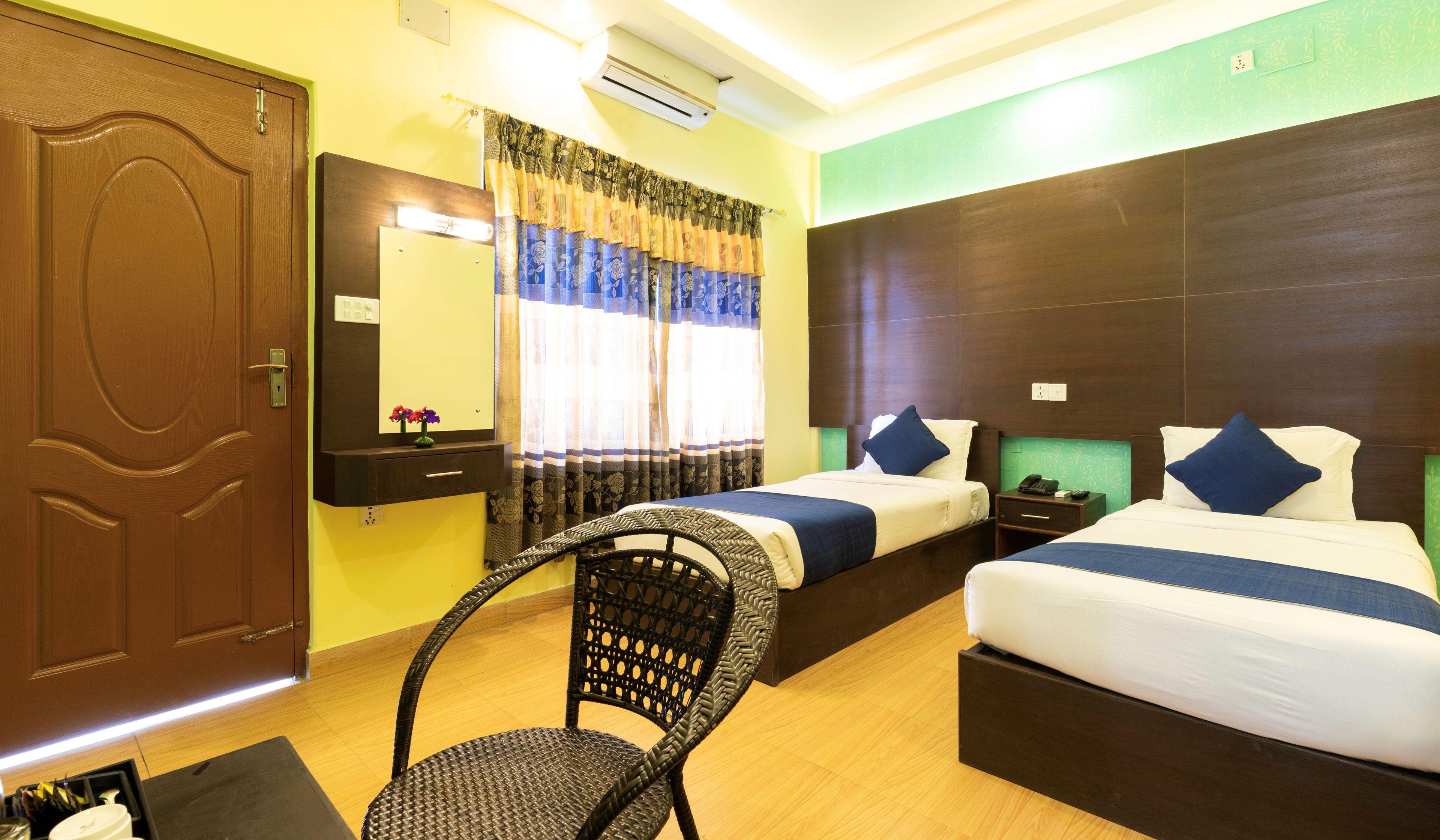 A hotel room with two beds, a chair, a bedside table, and a mirror.
