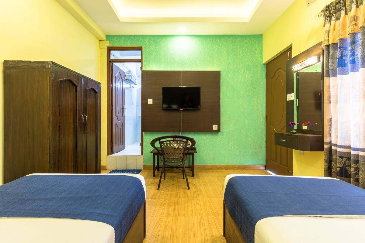 A hotel room with two beds, a TV mounted on the wall, a wooden wardrobe, and a chair.