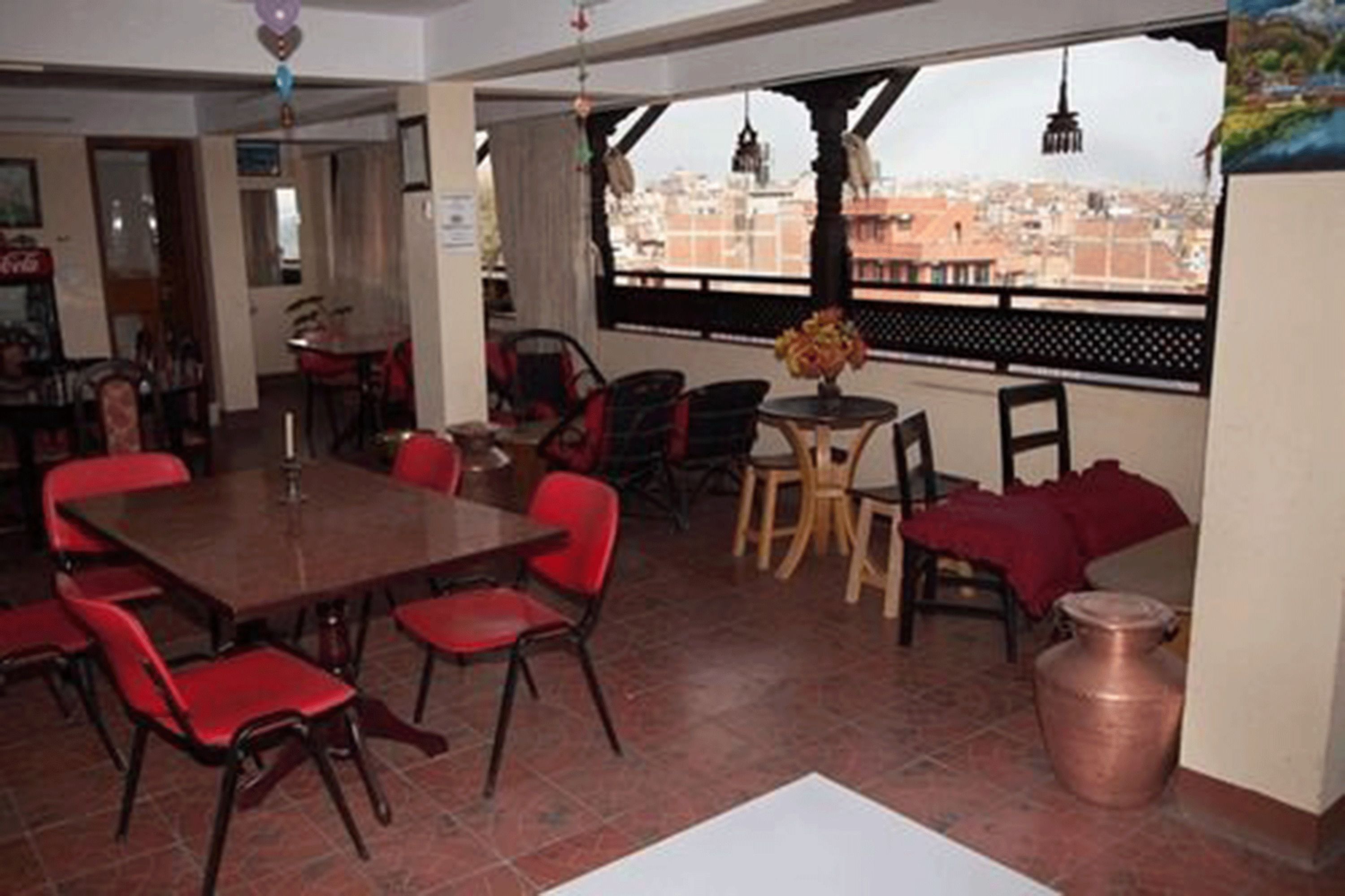 A dining area with a large table and red chairs, a small round table with a vase, and a view of the city through a window.