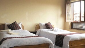A room with two single beds, each with a pillow and a blanket. There is a window with a view of buildings outside. - Heart of Bhaktapur (Bhaktapur)