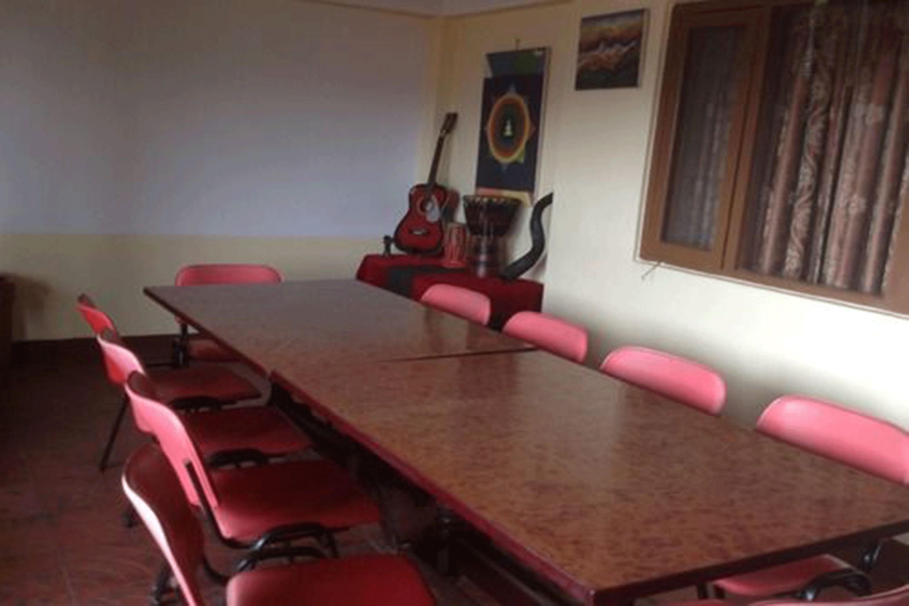 Una sala conferenze con un lungo tavolo e sedie rosse. Si nota una chitarra e un oggetto decorativo appeso al muro.