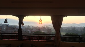 A room with a view of a cityscape at sunset, featuring a hanging light fixture and a patterned railing. - Heart of Bhaktapur (Bhaktapur)