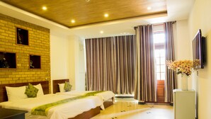 A hotel room with a brick accent wall, a large bed with two pillows, a small table, and a TV mounted on the wall. - Xuan Hung Hotel (Da Nang)