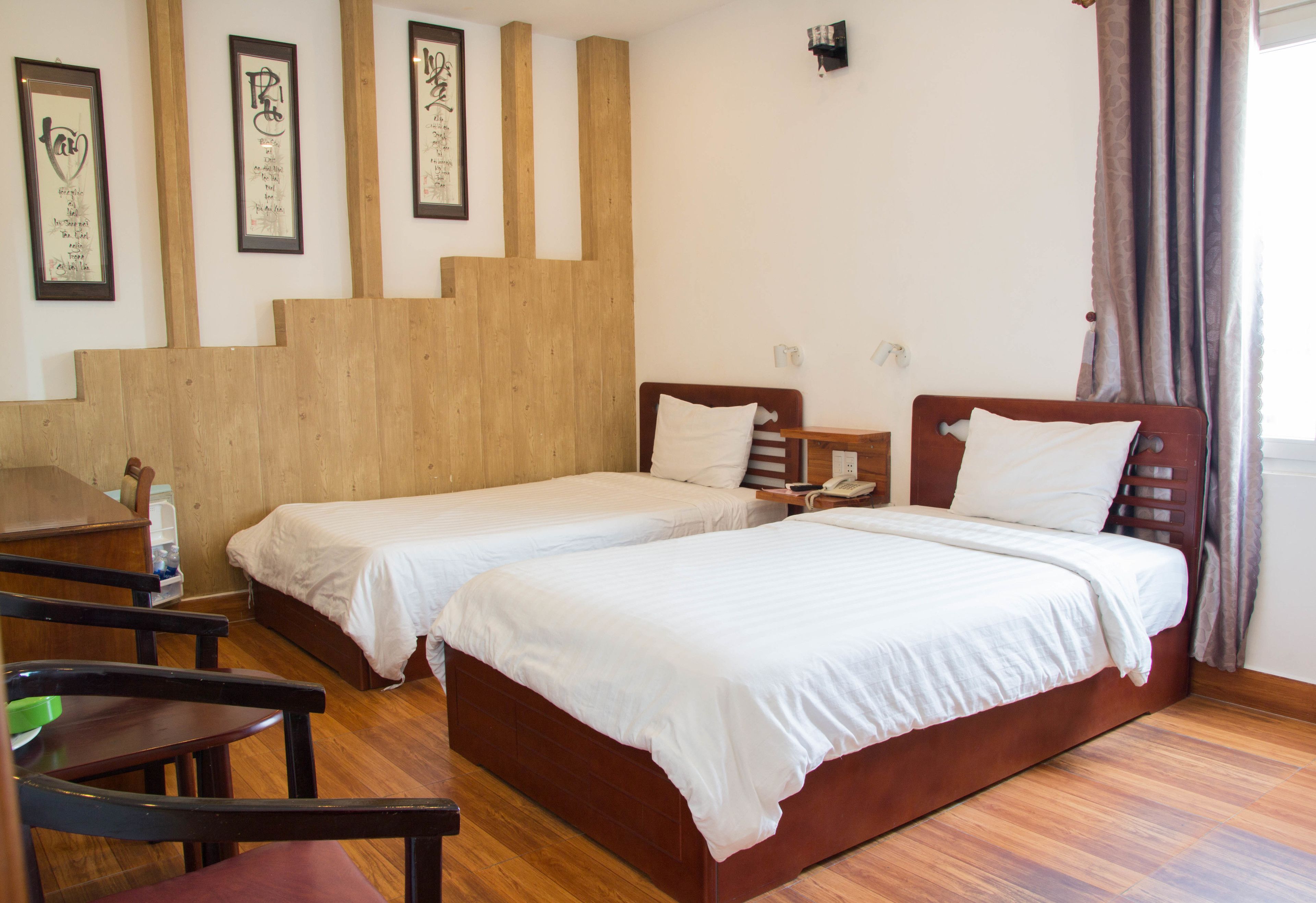 A room with two beds, wooden flooring, a desk, chairs, and framed artwork on the wall.