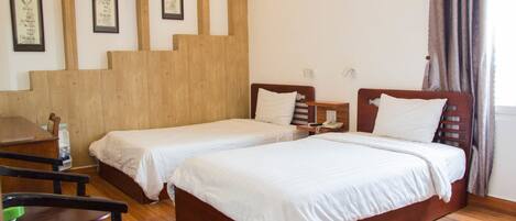 A room with two beds, wooden flooring, a desk, chairs, and framed artwork on the wall.