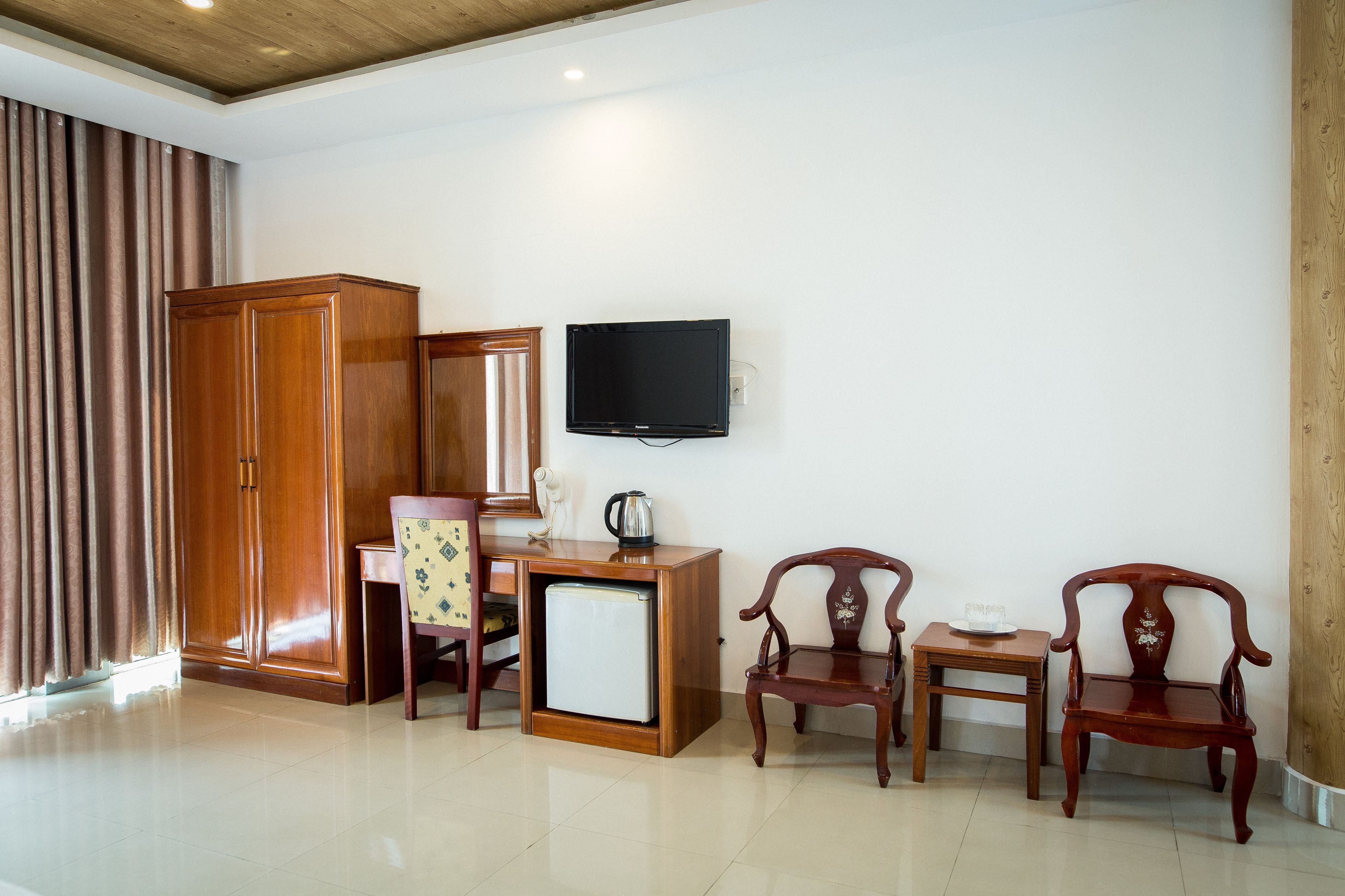 Una habitación con un armario de madera, un escritorio pequeño de madera con televisor, dos sillas de madera y un mueble de madera grande.