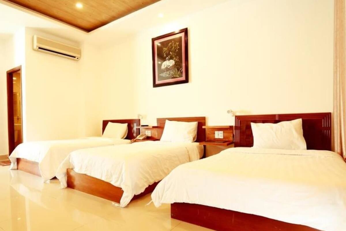 A hotel room with three single beds, wooden headboards, white bedding, and a framed picture on the wall.