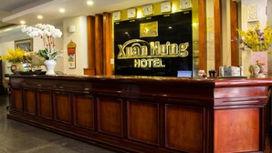 A reception desk with a sign for Xuan Huo Hotel, featuring a clock, a framed certificate, and a vase with flowers. - Xuan Hung Hotel (Da Nang)