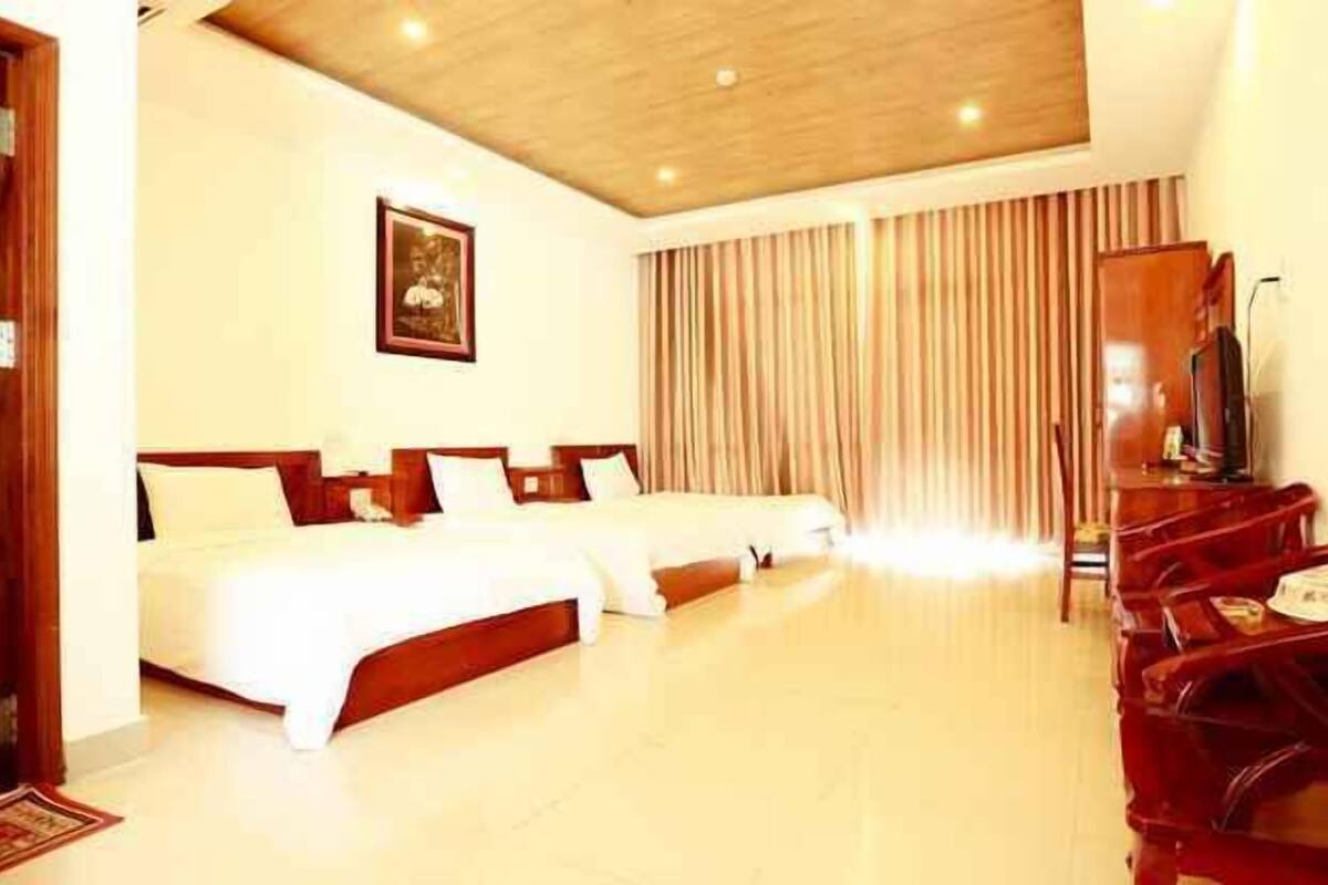 A hotel room with a large bed, a television, and a wooden cabinet.