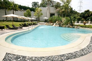 A swimming pool with lounge chairs and umbrellas, surrounded by rocks and greenery. - Le Beau Max Resort (Fanlu)