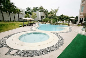 A swimming pool area with two circular pools, lounge chairs, umbrellas, and a green artificial turf section. - Le Beau Max Resort (Fanlu)
