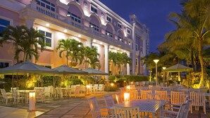 An outdoor dining area with tables and chairs, palm trees, and a building with balconies. - Le Beau Max Resort (Fanlu)