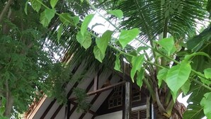 A two-story building with a balcony, surrounded by lush greenery and flowering plants. - Panji Panji Tropical Wooden Home (Langkawi)