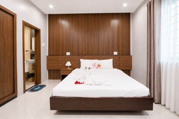 A modern hotel room with a wooden headboard, a large bed, a nightstand with a lamp, and a view of the bathroom. - BeSea Hotel Da Nang (Da Nang)