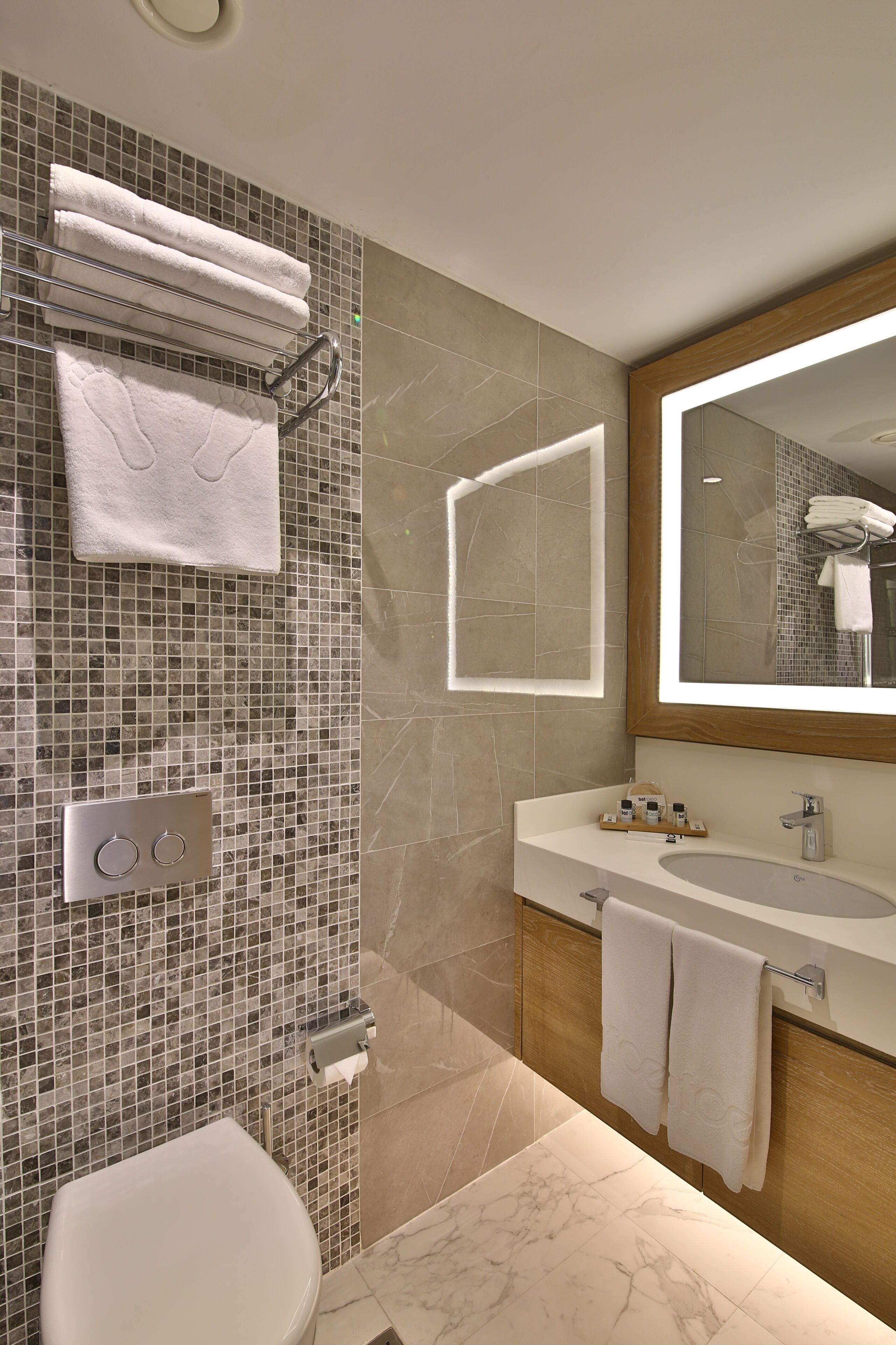 A modern bathroom with a tiled backsplash, a large mirror, a sink with a vanity, and a toilet.