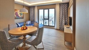Una sala de estar moderna con comedor, un conjunto de sofás, un televisor de pantalla plana y vista a la ciudad a través de amplias ventanas.