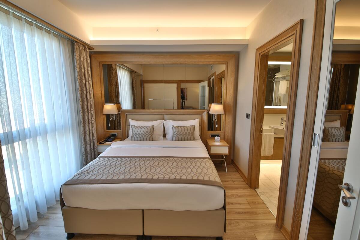 A hotel room with a large bed, bedside tables, a mirror, and a bathroom visible through an open door.