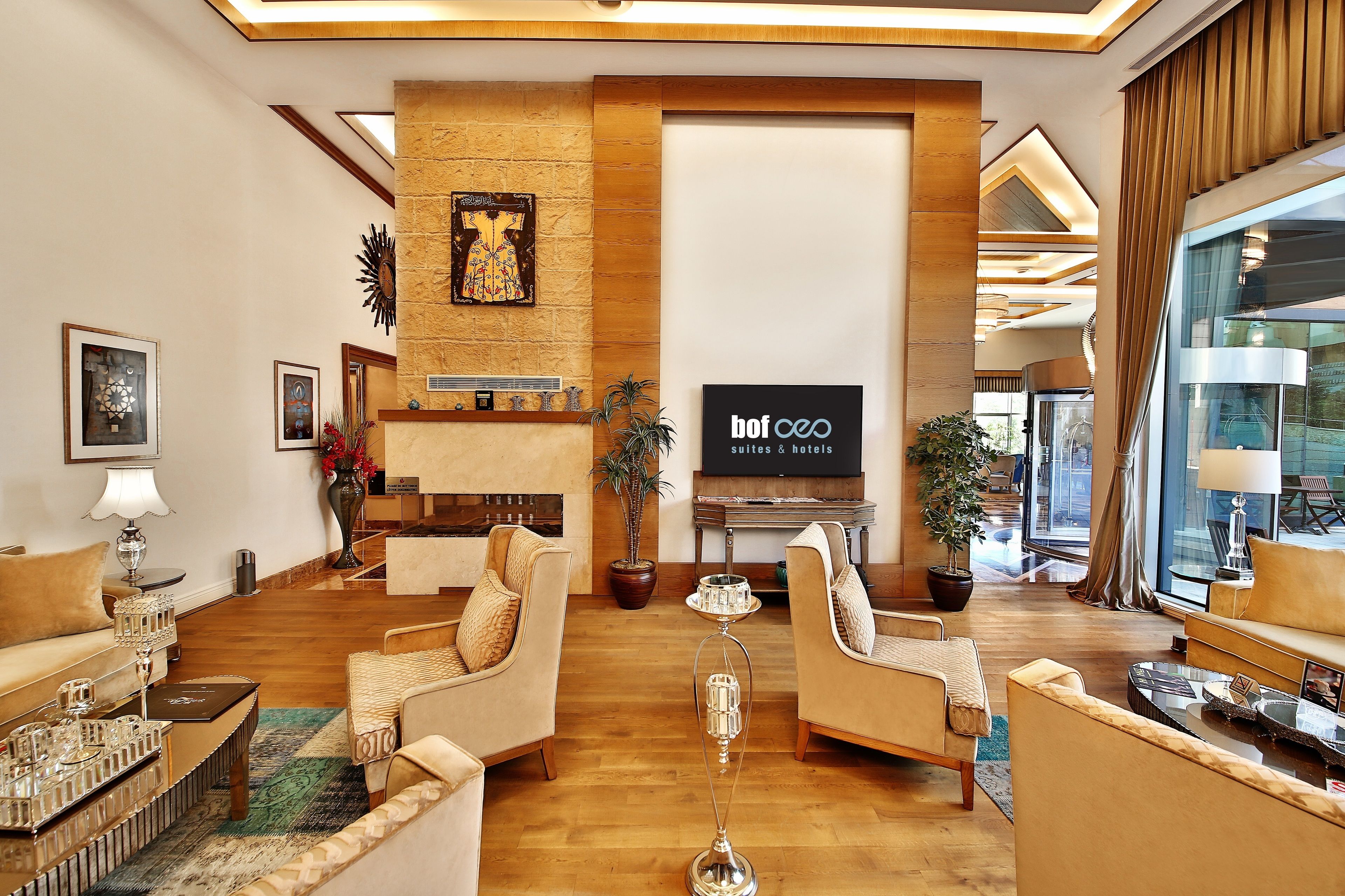 A spacious hotel lobby with a modern design, featuring a large TV screen, comfortable seating, and a fireplace.