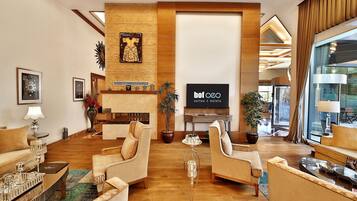 A spacious hotel lobby with a modern design, featuring a large TV screen, comfortable seating, and a fireplace.
