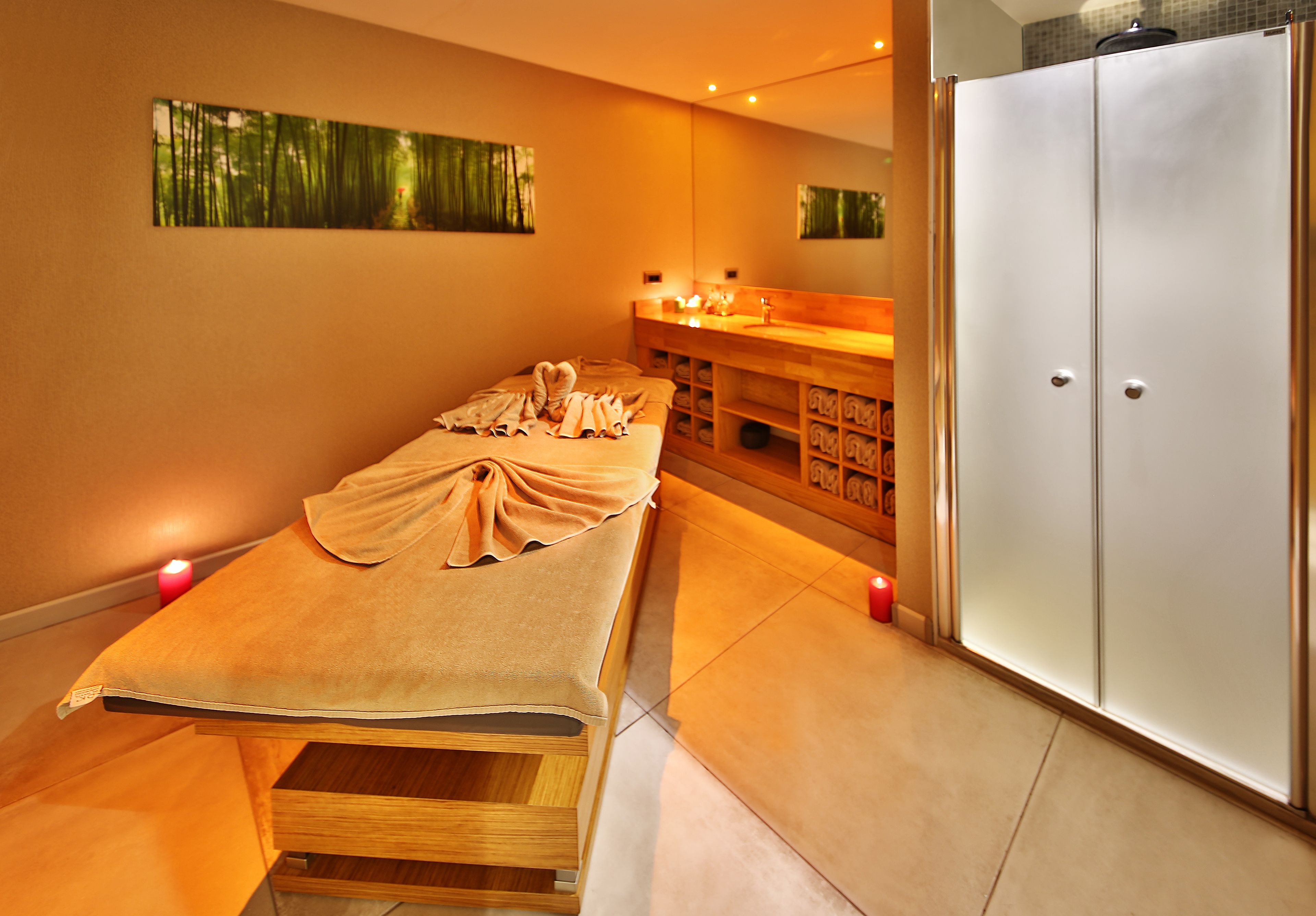 Une salle de spa équipée d’une table de massage, d’un meuble en bois contenant des serviettes et d’une grande armoire.