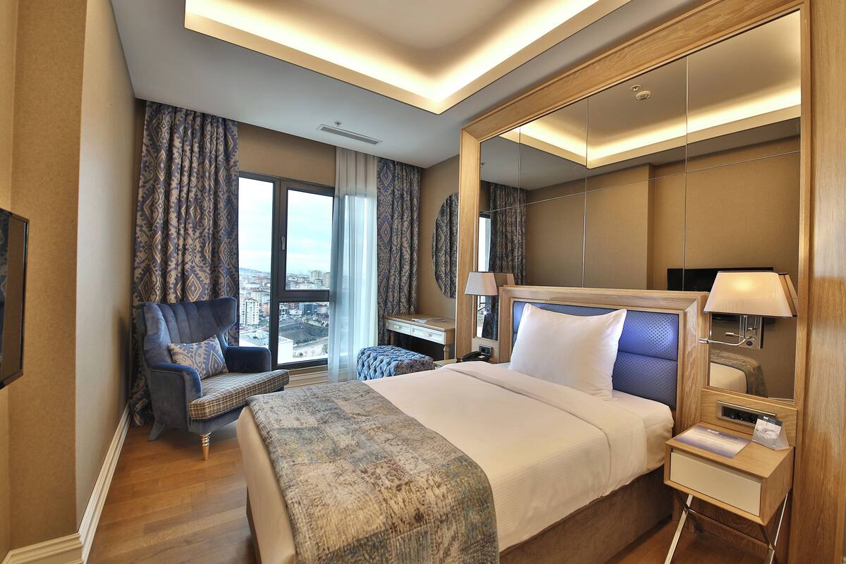 A hotel room with a large bed, a desk, a chair, and a large mirror.
