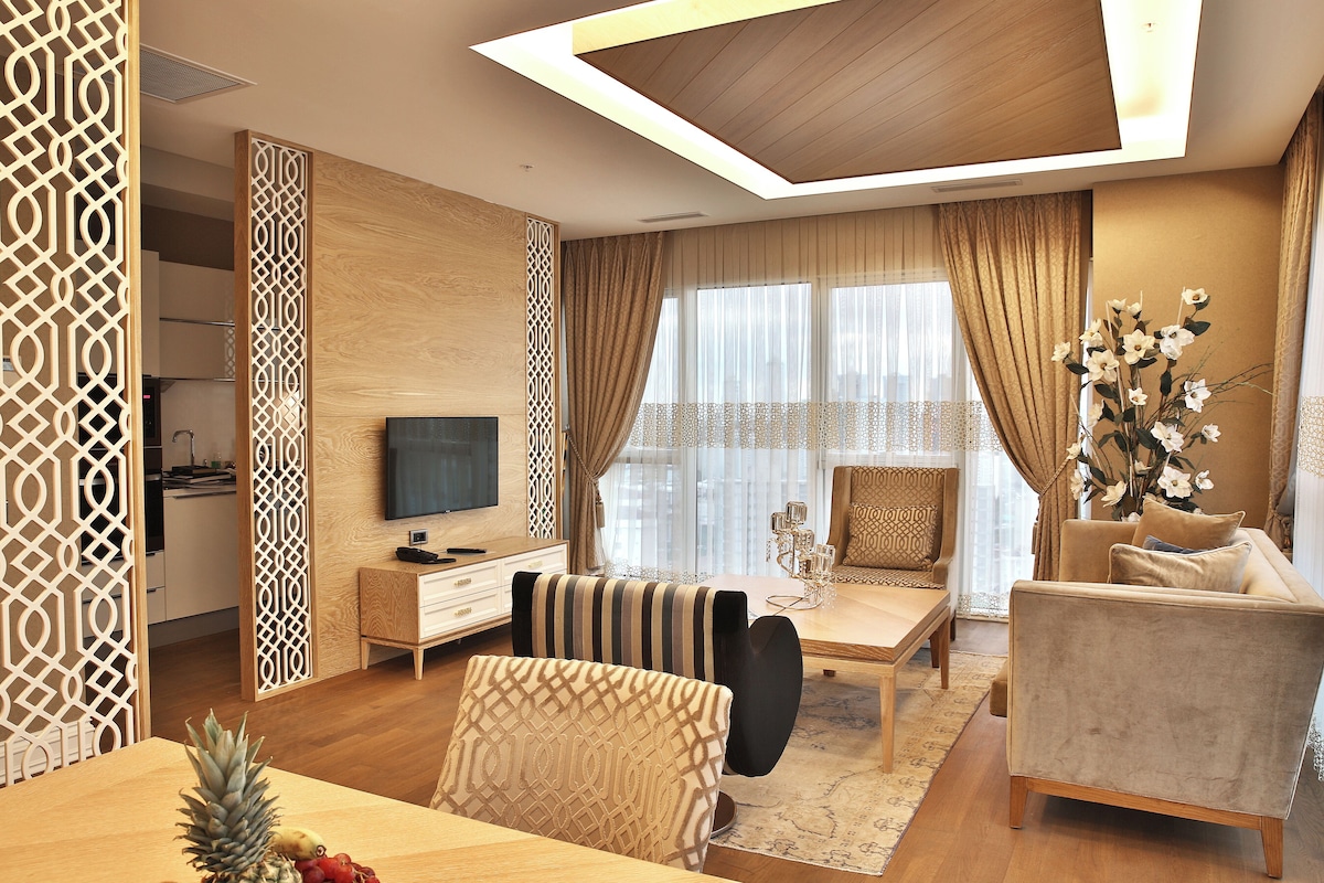 A modern living room with a wooden ceiling, a TV, a sofa, a dining table with fruit, and a decorative plant.