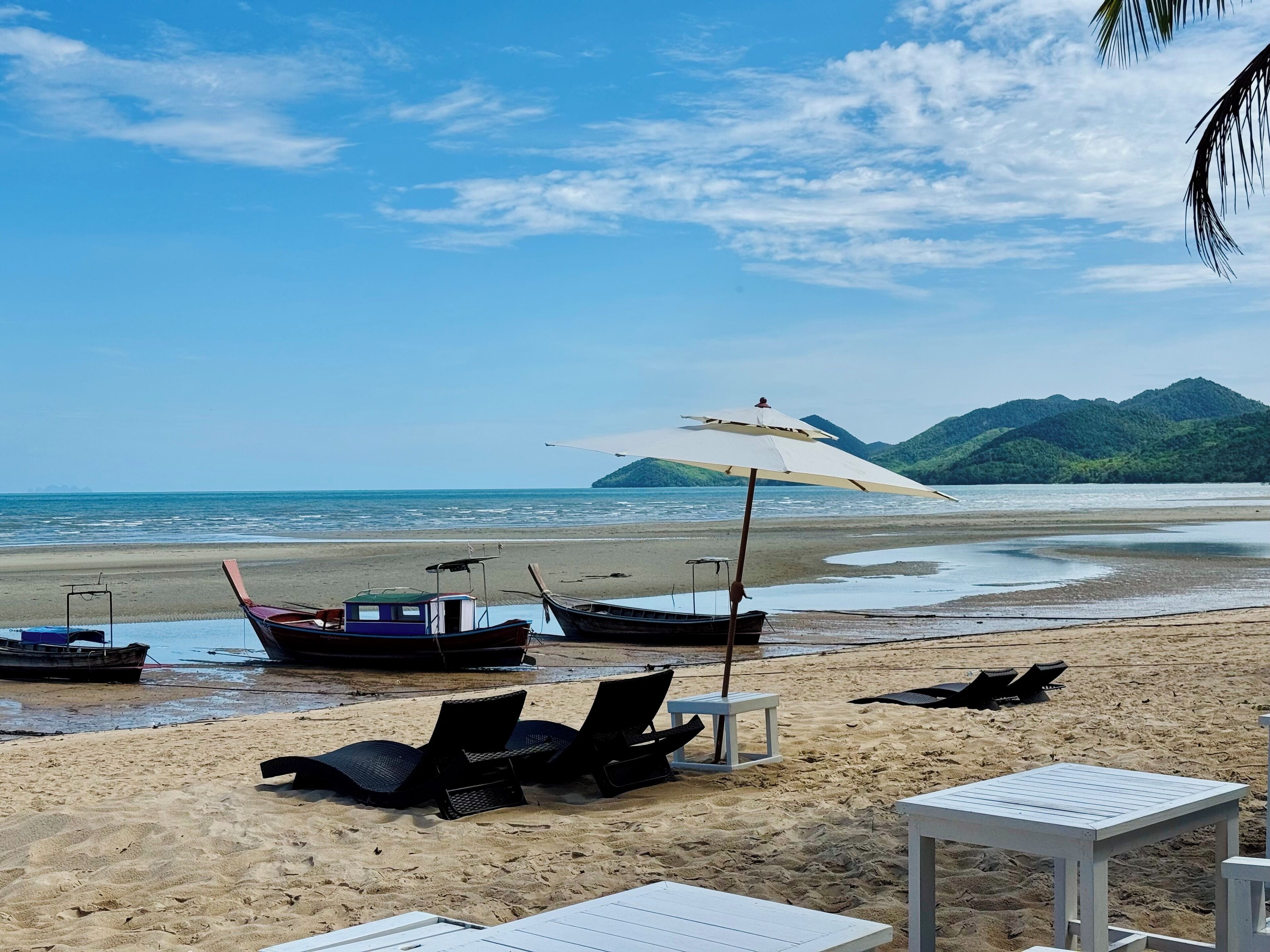 A beach with lounge chairs, a table, and a boat under an umbrella.