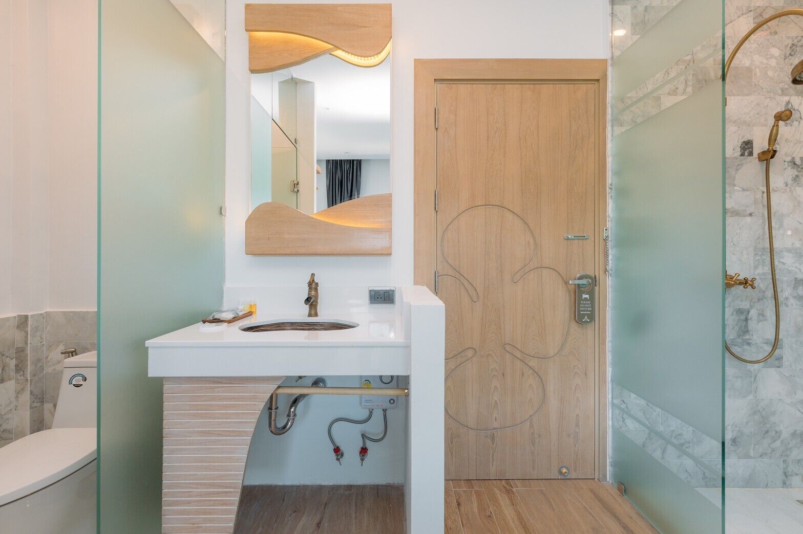 A modern bathroom with a wooden door, a white sink, and a glass shower enclosure.