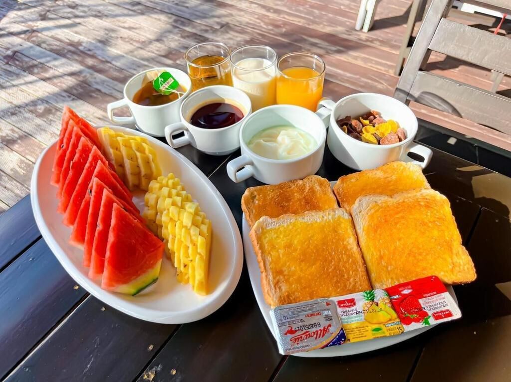 Une table de petit-déjeuner avec des tranches de pastèque, du maïs, des toasts et diverses boissons.