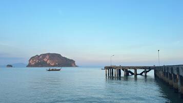 A calm sea with a pier extending into it, a boat, and a large rocky island in the background.