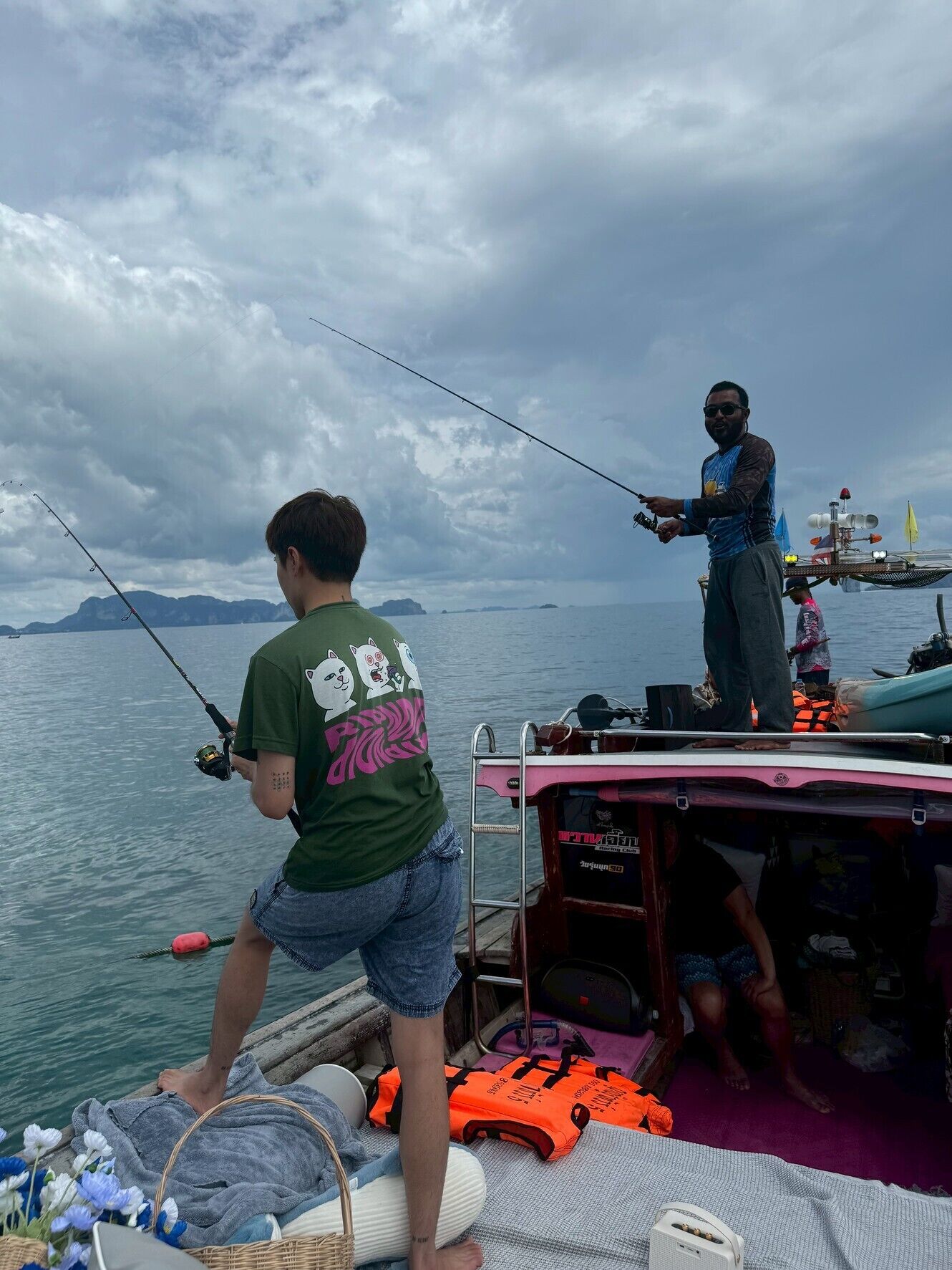 A boat with two people fishing, a life jacket, and a speaker on the deck.