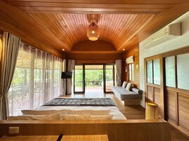 Habitación de hotel con cama, sofá, televisión y balcón con vistas a zonas verdes.