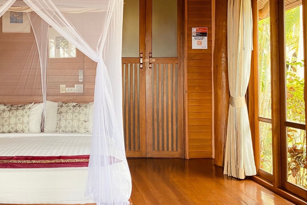 A room with a bed under a canopy, wooden walls, and a window with curtains.