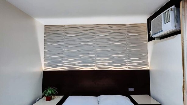 A bedroom with a bed, a nightstand, a potted plant, and a wall-mounted air conditioner. - Bamboo Garden Business Inn (Dipolog)