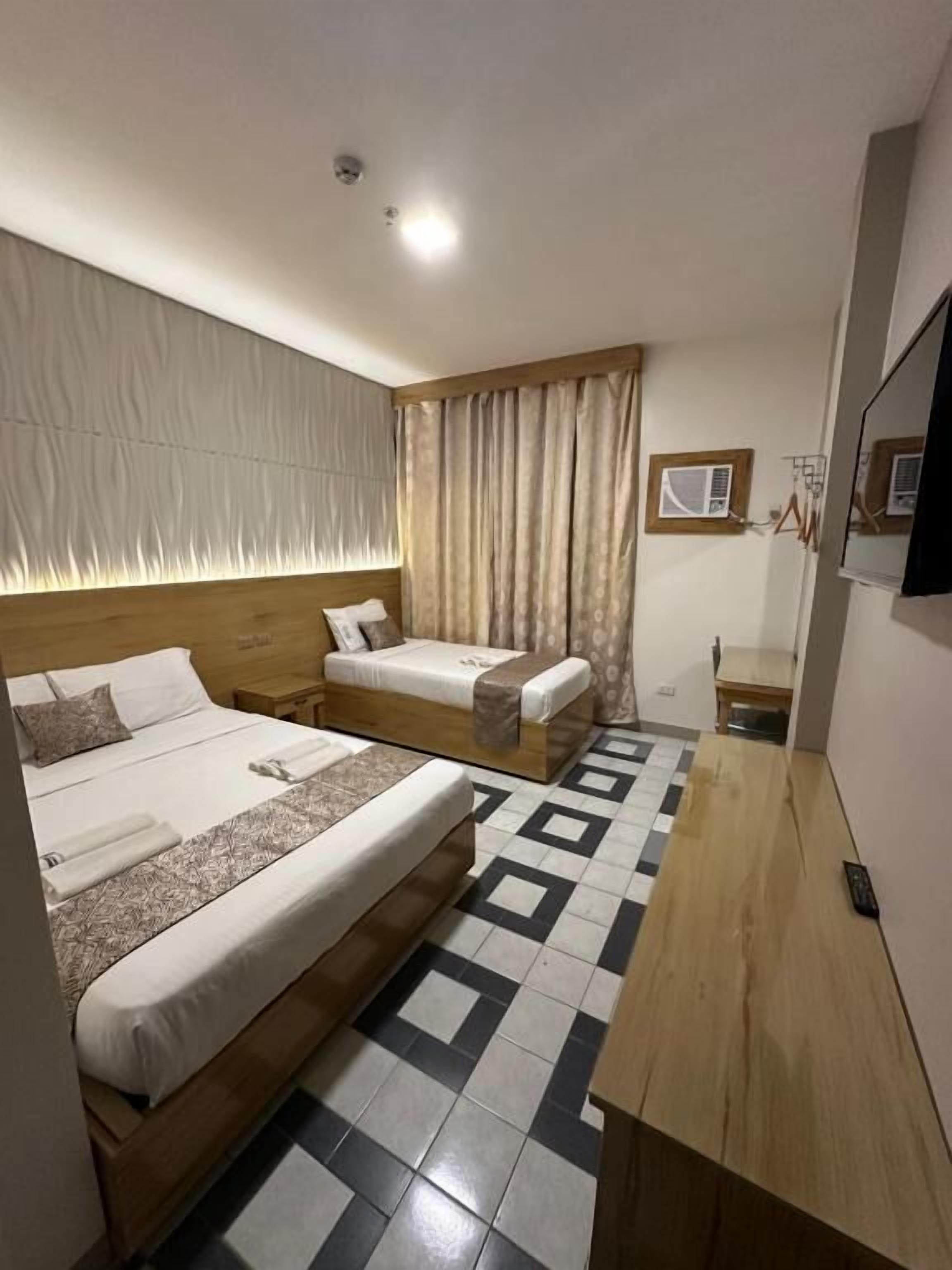 A hotel room with two beds, a wooden nightstand, a small table, a TV, and a patterned floor.