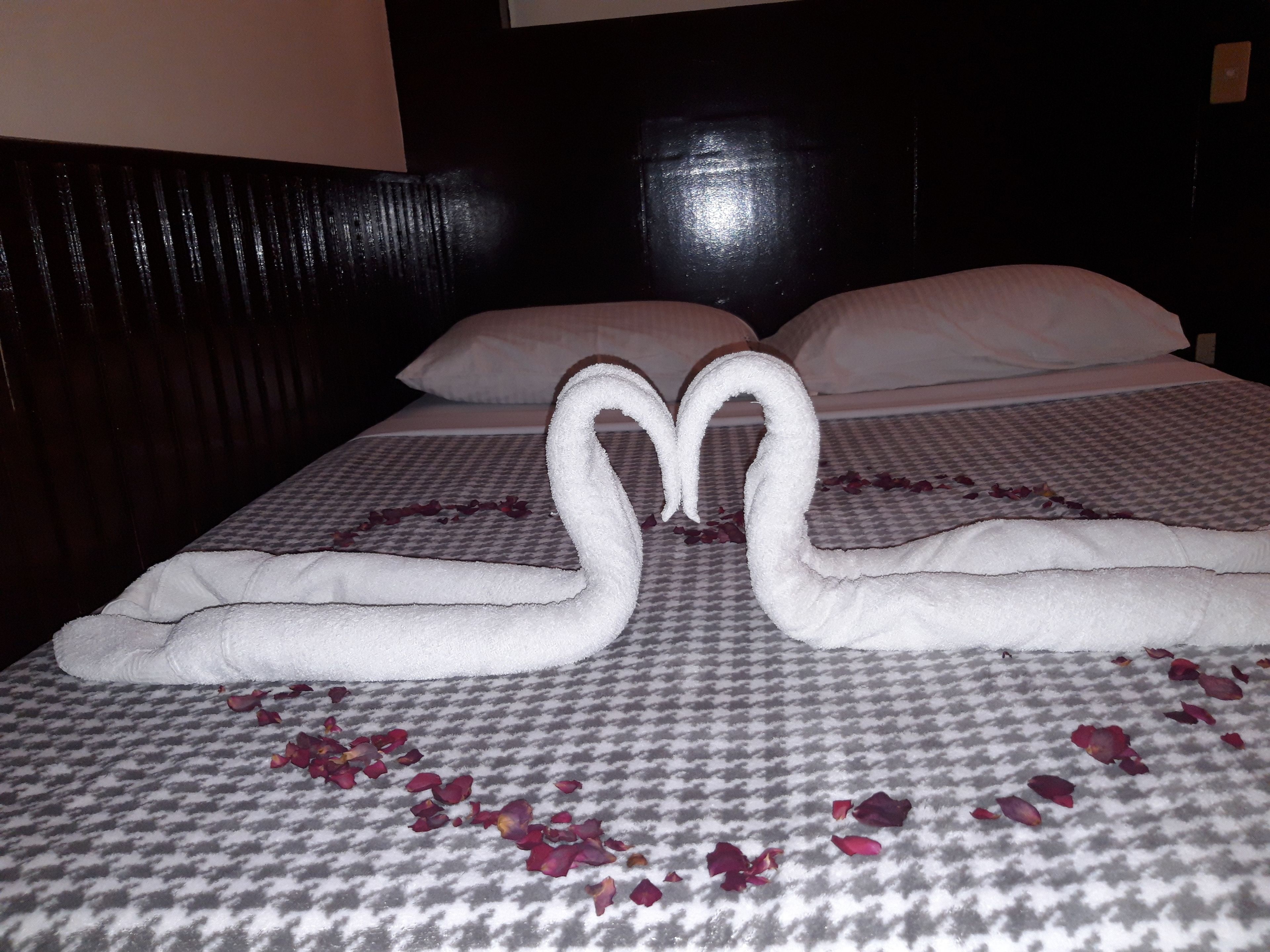 Un lit recouvert d’une couverture à carreaux, avec deux serviettes disposées de manière à évoquer des cygnes.