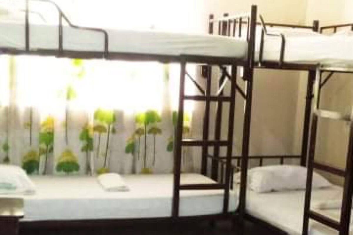 A dormitory room with bunk beds, a tiled floor, and a window with curtains.