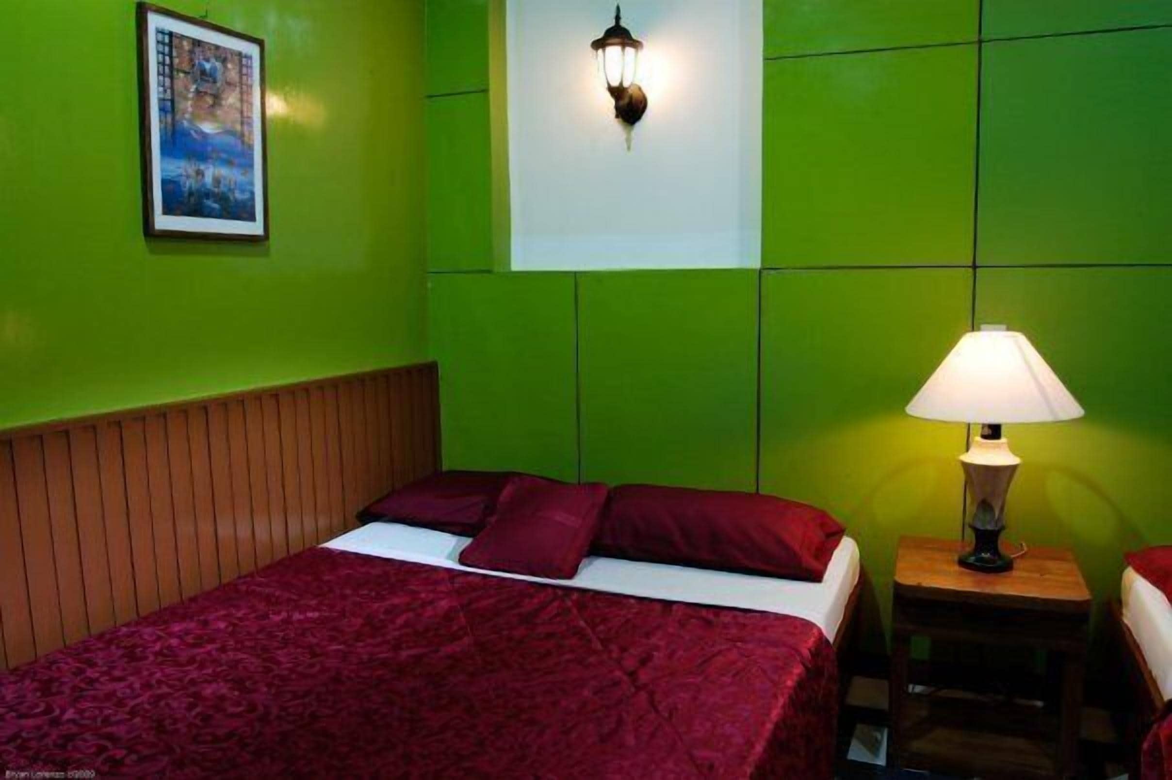 Una habitación con una cama, una mesita de noche, una lámpara de pared y un cuadro enmarcado.