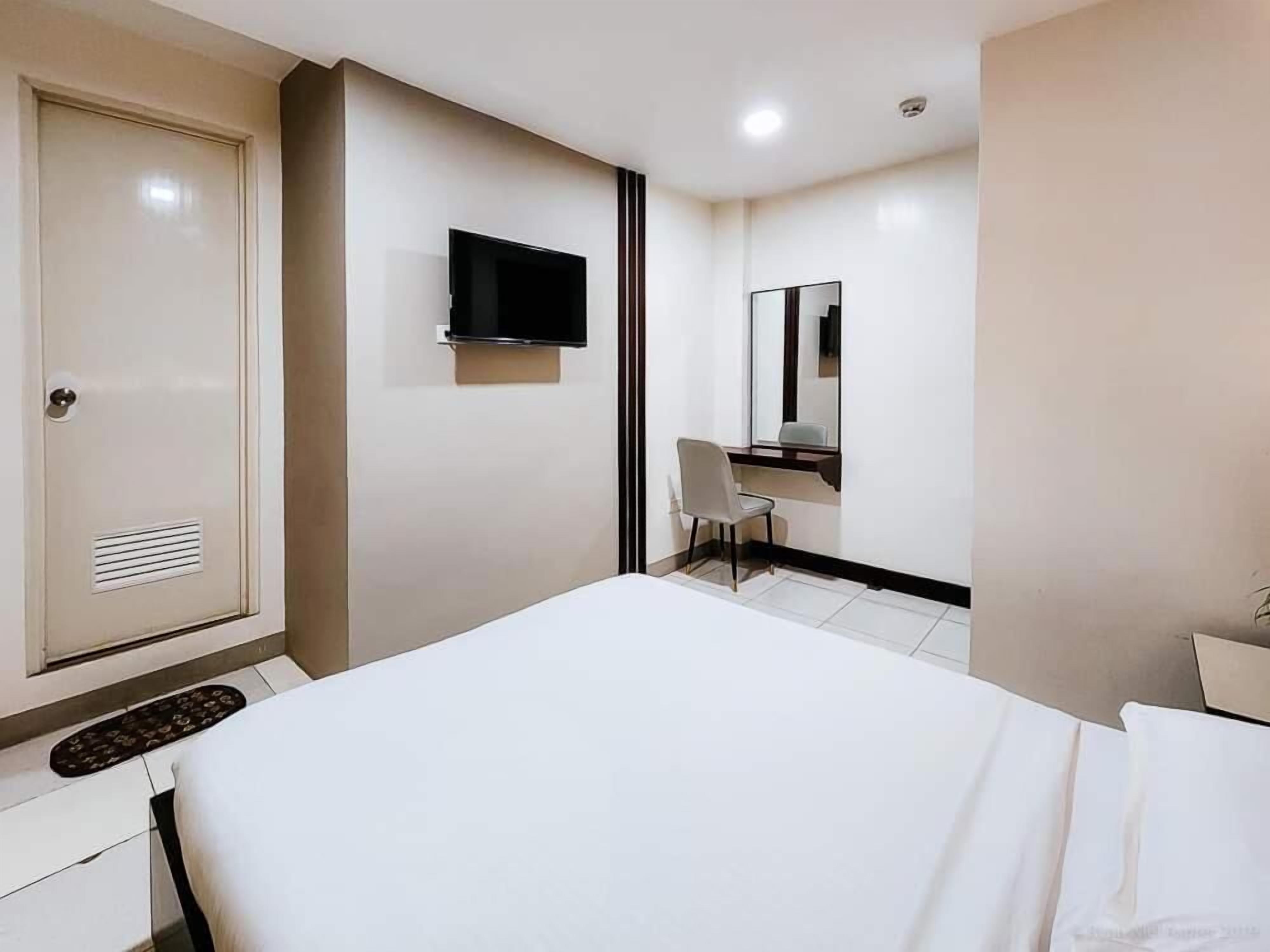 Una habitación de hotel con cama, escritorio, silla, televisor y espejo.