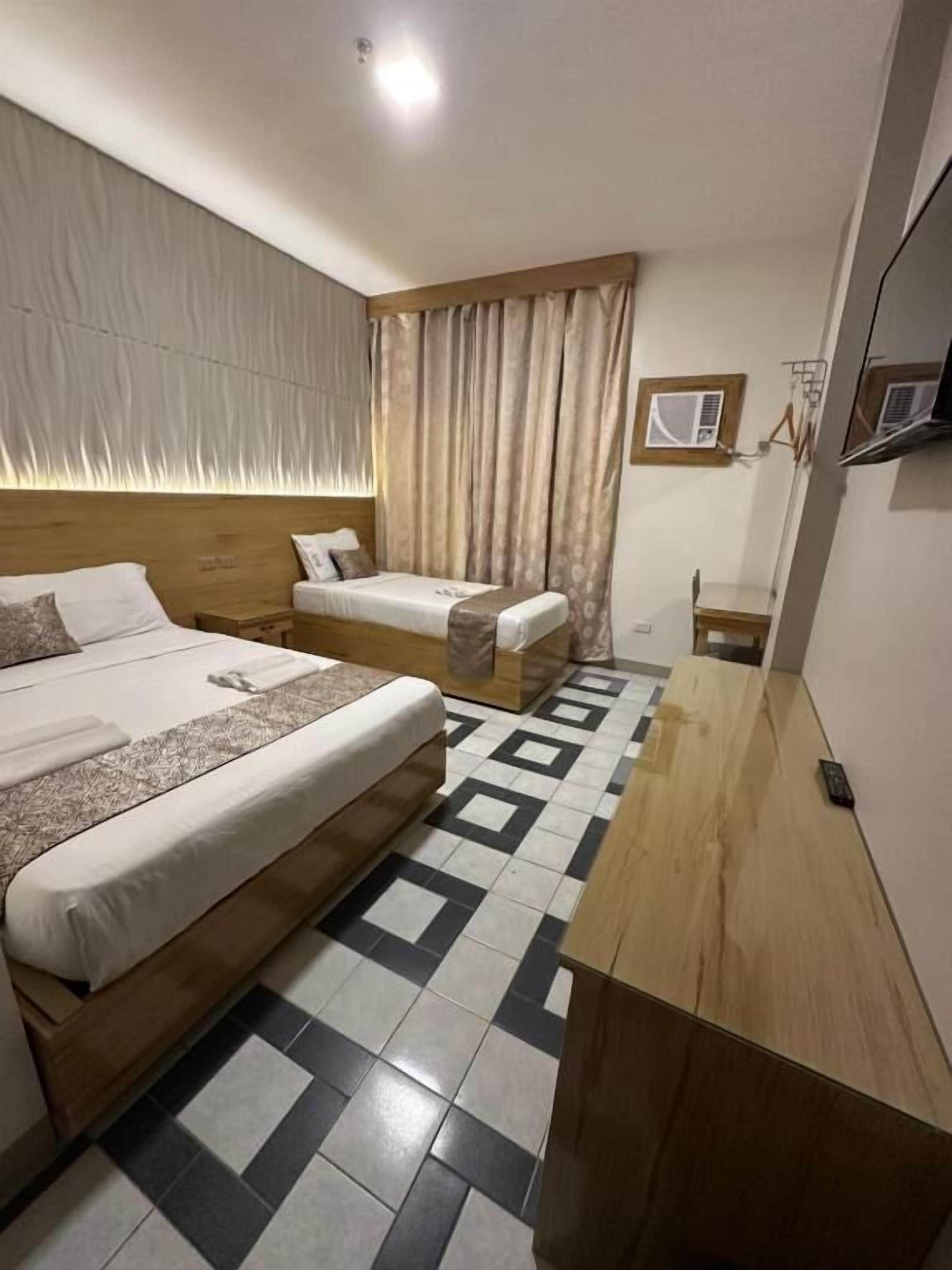 Una habitación de hotel con una cama grande, una cama más pequeña, un escritorio de madera y un suelo estampado.