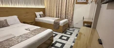 Una habitación de hotel con una cama grande, una cama más pequeña, un escritorio de madera y un suelo estampado.