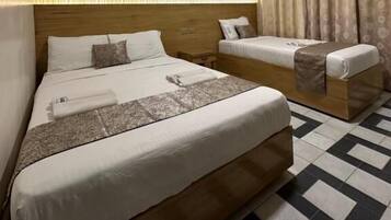 Una habitación de hotel con una cama grande, otra más pequeña, un cabecero, una mesita de noche y una cortina.