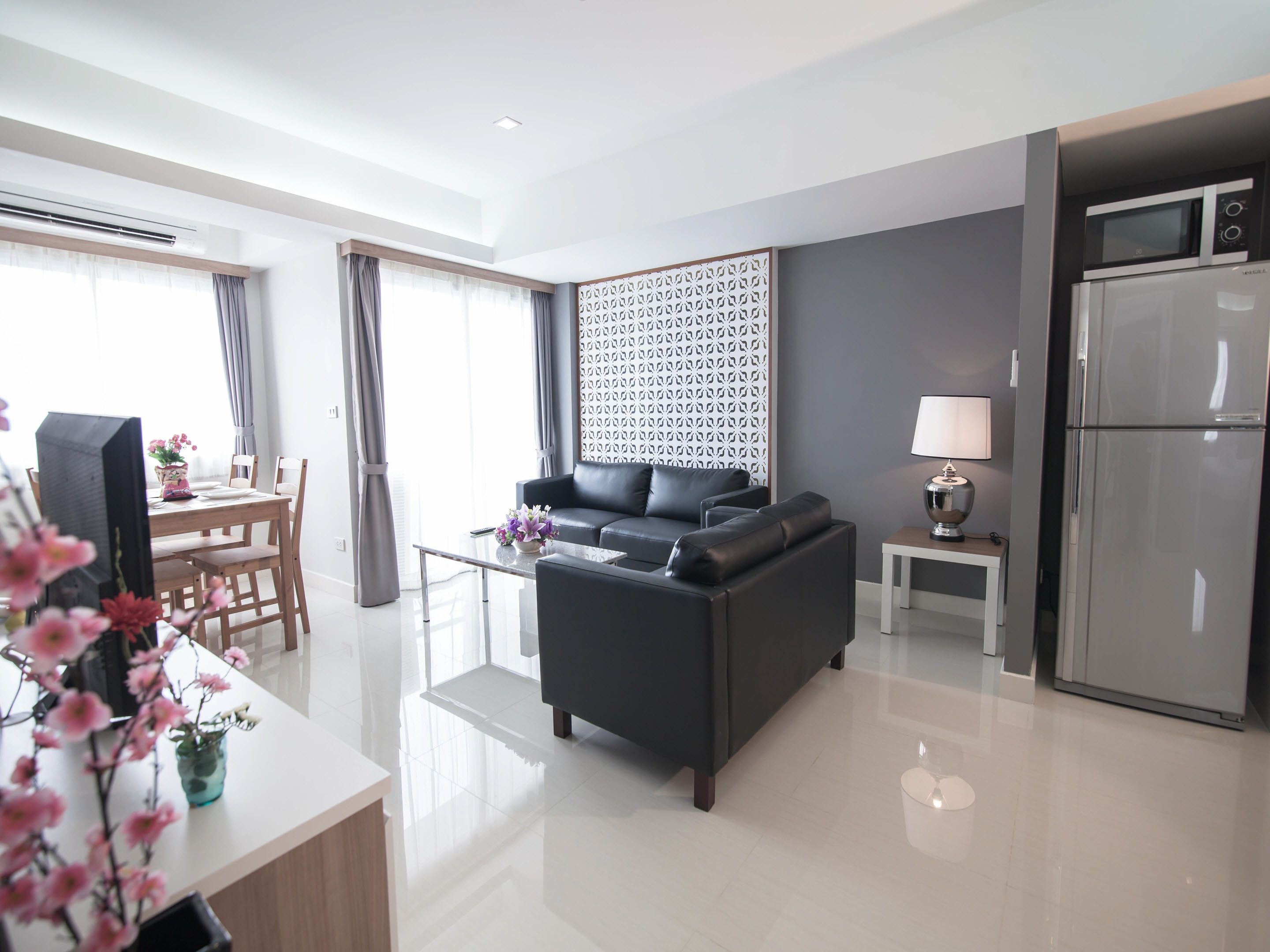 A modern living room with a sofa, a dining table with chairs, a small side table with a lamp, and a refrigerator.