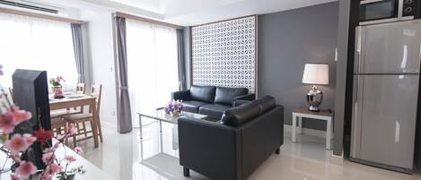 Un salon moderne comprenant un canapé, une table à manger avec des chaises, une petite table d’appoint avec une lampe et un réfrigérateur.