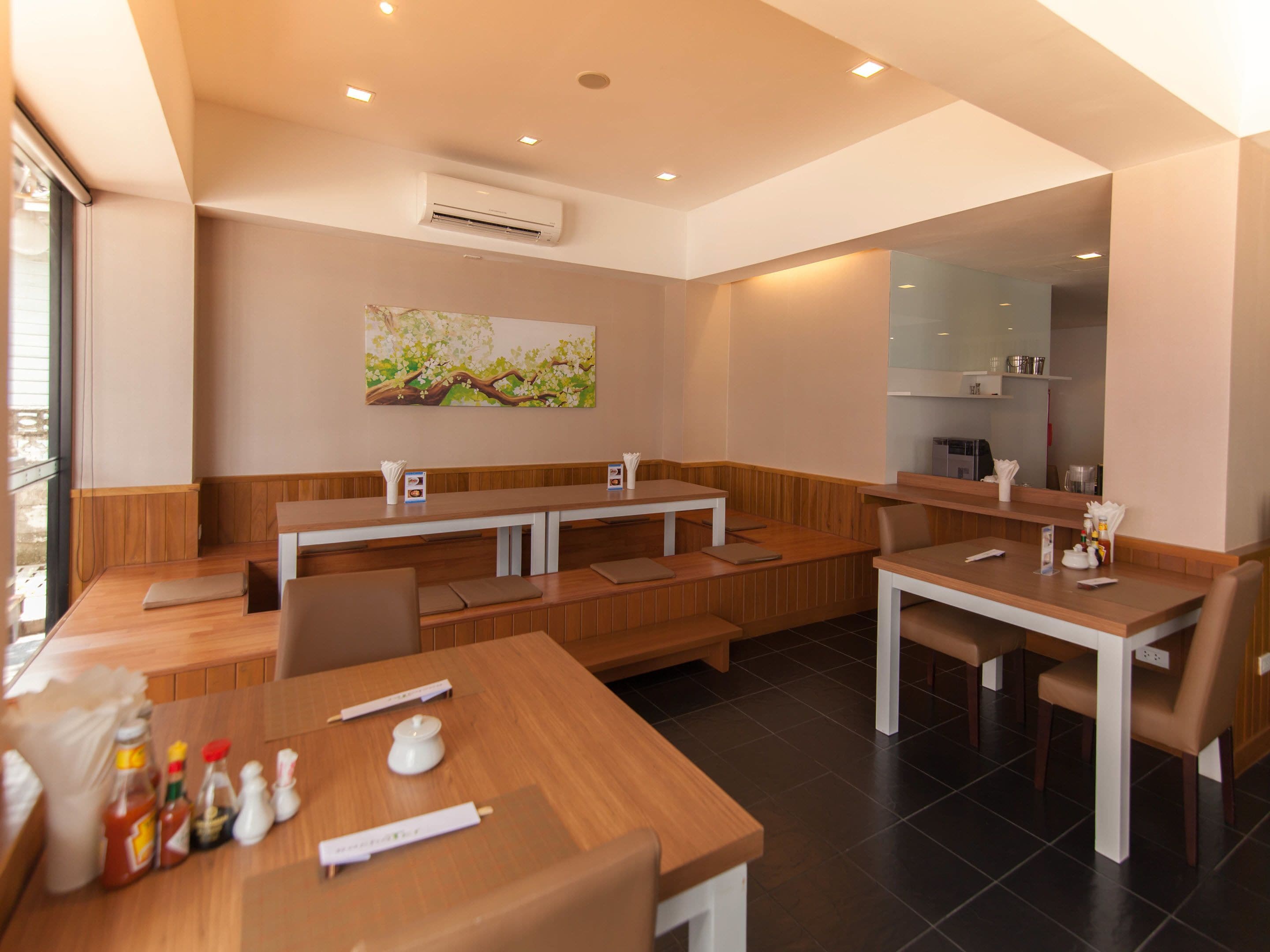 Un restaurante moderno con mesas y bancos de madera, un equipo de aire acondicionado y un cuadro en la pared.
