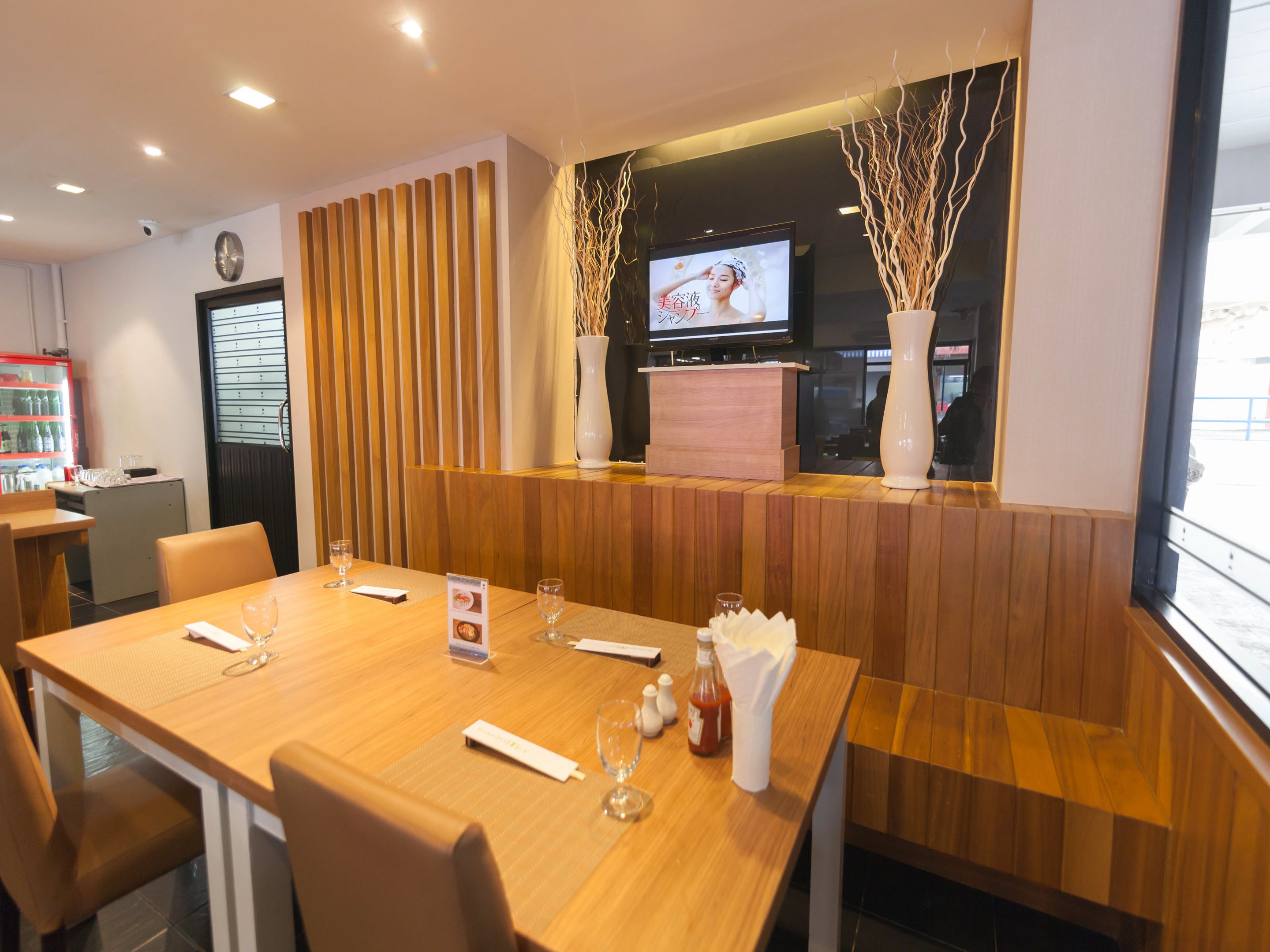 Un restaurante con una mesa de madera, sillas, una pantalla de televisión y un jarrón decorativo.