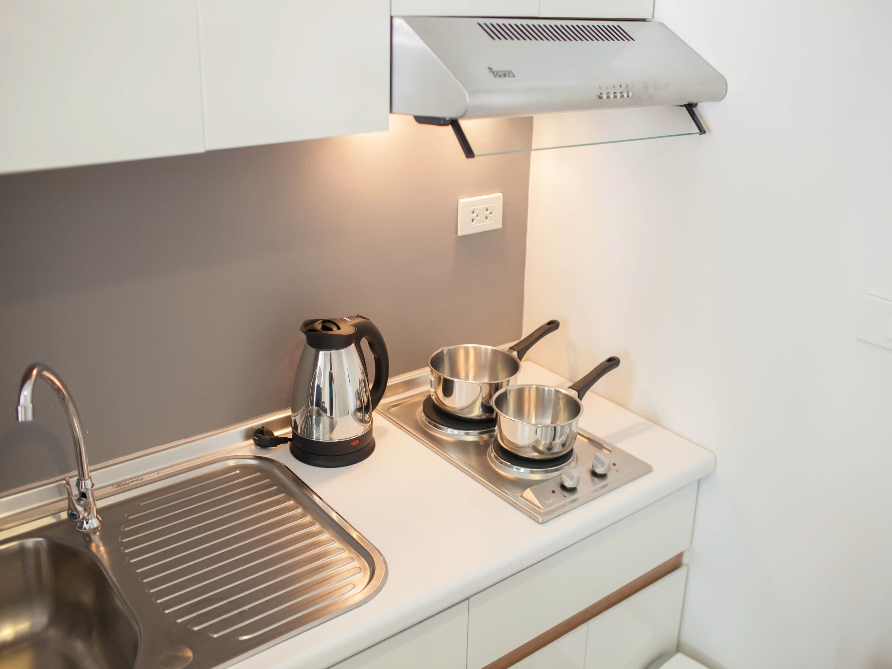 Una cocina moderna con un lavamanos de acero inoxidable, una tetera y dos ollas sobre una hornilla.
