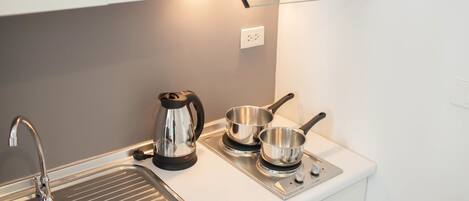Una cocina moderna con un lavamanos de acero inoxidable, una tetera y dos ollas sobre una hornilla.