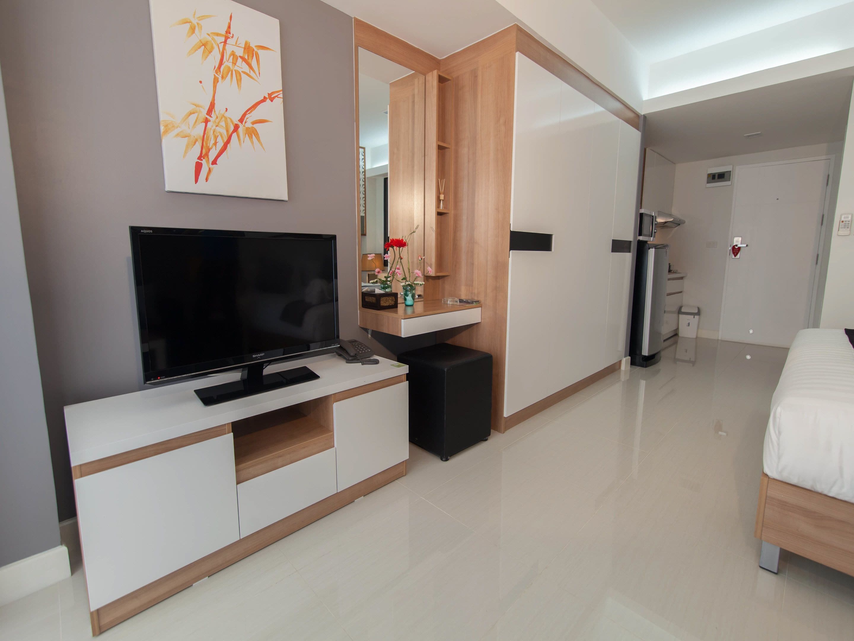 A modern hotel room with a flat-screen TV, a wooden cabinet, a mirror, a bed, and a toilet.