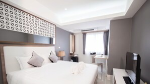 Ein modernes Hotelzimmer mit einem großen Bett, einem Schreibtisch, einem Fernseher und einem Fenster mit Vorhängen.